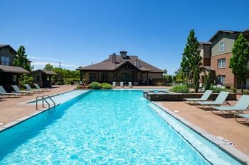 A large swimming pool in front of a house with a brown roof.